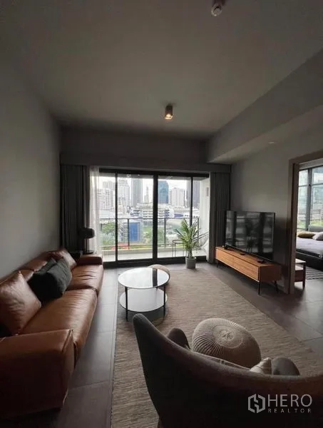 Condominium for rent in Watthana, Bangkok - Modern living room with leather sofa, TV console and balcony city view.