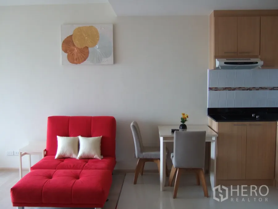 公寓 出租在Khlong Toei, Bangkok - 明亮客厅，红色沙发躺椅、双人餐桌与紧凑厨房柜。