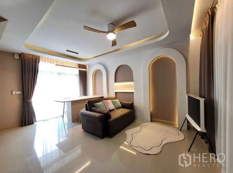Townhouse for rent or sale - Stylish living room with curved recessed niches, ceiling fan, sofa, TV and floor-to-ceiling curtains.