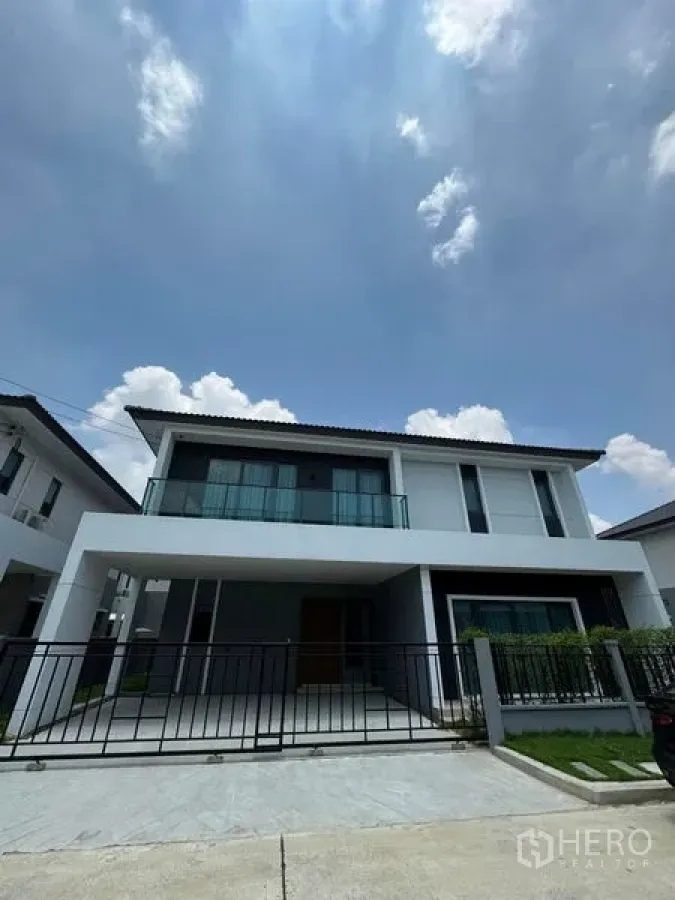 Detached House for rent in Don Mueang, Bangkok - Front elevation of the white detached house featuring covered carport, metal fence and neat landscaping.