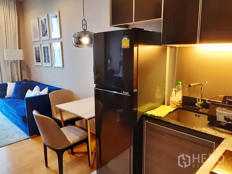 公寓 出租在Khlong Toei, Bangkok - 紧凑型厨房，黑色橱柜、双门冰箱和双人餐桌。