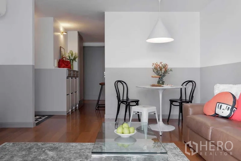 Condominium for sale in Watthana, Bangkok - Open-plan living and dining area with round table, leather sofa and glass coffee table.