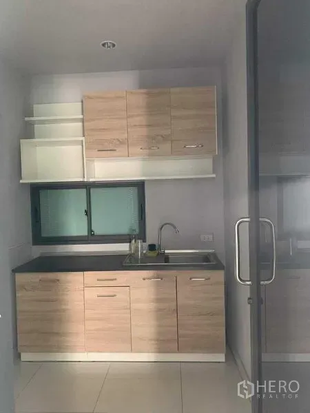 Townhouse for rent or sale in Yan Nawa, Bangkok - Compact kitchenette with light-wood cabinets, sink and small window behind glass door.