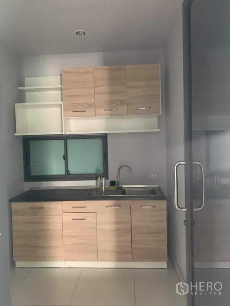 Townhouse for rent or sale in Yan Nawa, Bangkok - Compact kitchenette with light-wood cabinets, sink and small window behind glass door.