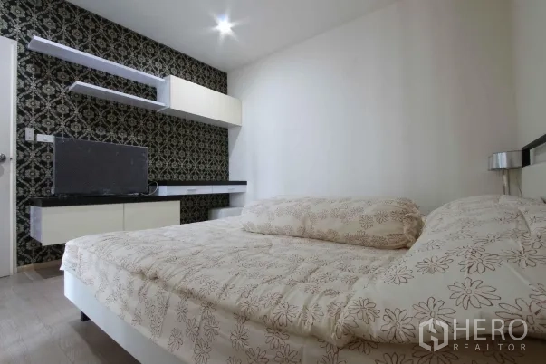 Condominium for rent in Khlong Toei, Bangkok - Cozy bedroom with patterned feature wall, floating shelves, TV console, and a queen bed in a Bangkok condominium.