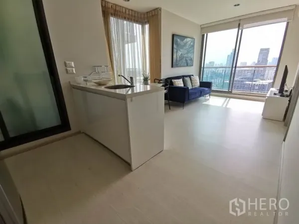 Condominium for rent in Khlong Toei, Bangkok - Open-plan kitchen with island facing a living area and floor-to-ceiling windows with skyline views.