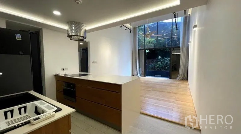Condominium for rent in Watthana, Bangkok - Modern kitchen with island and built-in oven looking toward the bright living room with tall windows.
