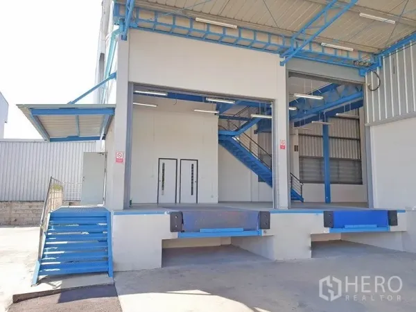 คลังสินค้า ให้เช่าในLat Krabang, Bangkok - ท่าขนถ่ายยกระดับพร้อมประตูม้วนและบันไดเหล็กสีน้ำเงินอยู่ใต้ชายคาหน้าโกดัง