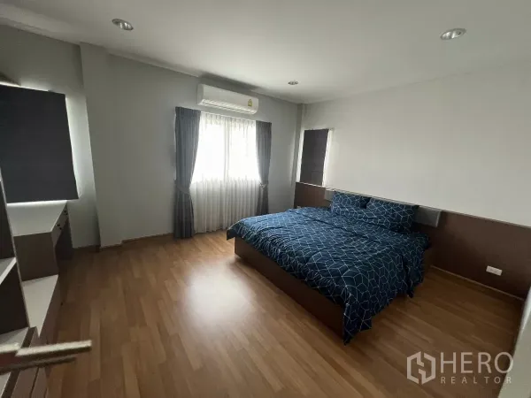 Detached House for rent or sale in Don Mueang, Bangkok - Spacious bedroom with double bed, wood floors, air conditioner and two curtained windows.