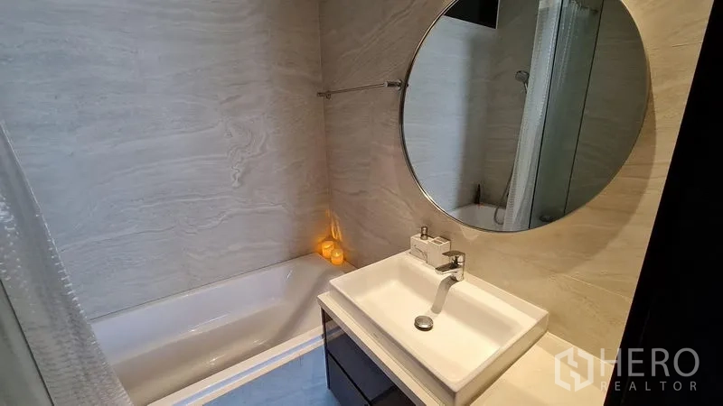 Condominium for rent - Bathroom with bathtub, round mirror and vanity set against light marble-look tiles.