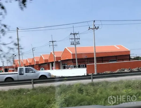 Warehouse for rent in Pathum Thani - Row of orange‑roof warehouse units with roadside access, power lines, and perimeter fencing in Lat Lum Kaeo, Pathum Thani.