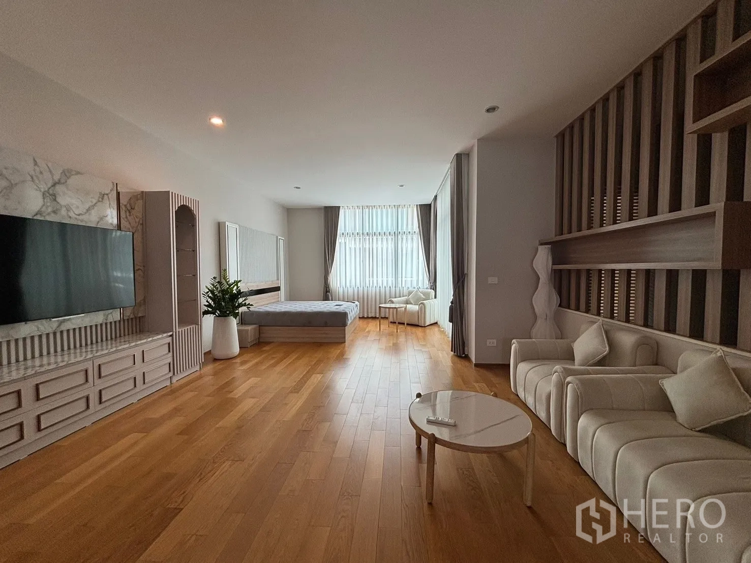 Townhouse for rent in Saphan Sung, Bangkok - Expansive suite with bed, sofas, TV wall, and a wide window.