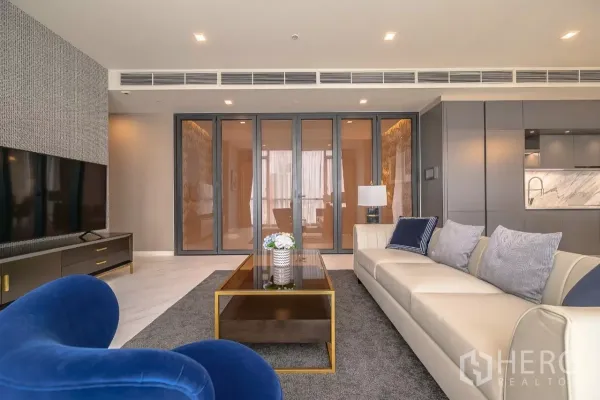 公寓 出租在Watthana, Bangkok - 客厅望向折叠玻璃门与大理石背墙厨房，灯光柔和。