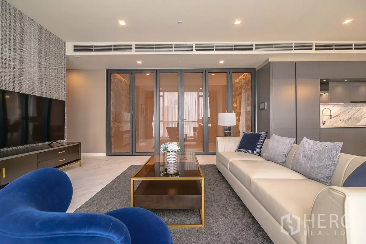 公寓 出租在Watthana, Bangkok - 客厅望向折叠玻璃门与大理石背墙厨房，灯光柔和。