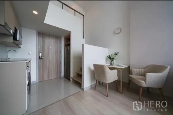 Condominium for rent in Sathon, Bangkok - Compact kitchen and dining nook under a loft with a wooden entry door.