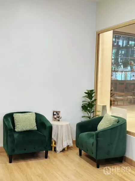 零售空间 出租 - 等候区，两把绿色绒面单人沙发、边几与绿植，旁有玻璃隔断。