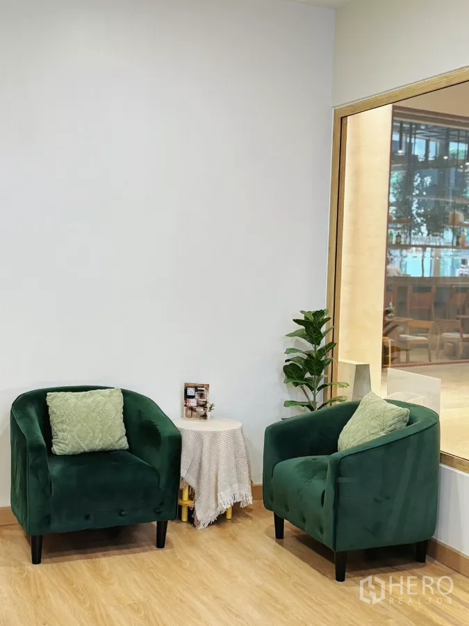 零售空间 出租 - 等候区，两把绿色绒面单人沙发、边几与绿植，旁有玻璃隔断。