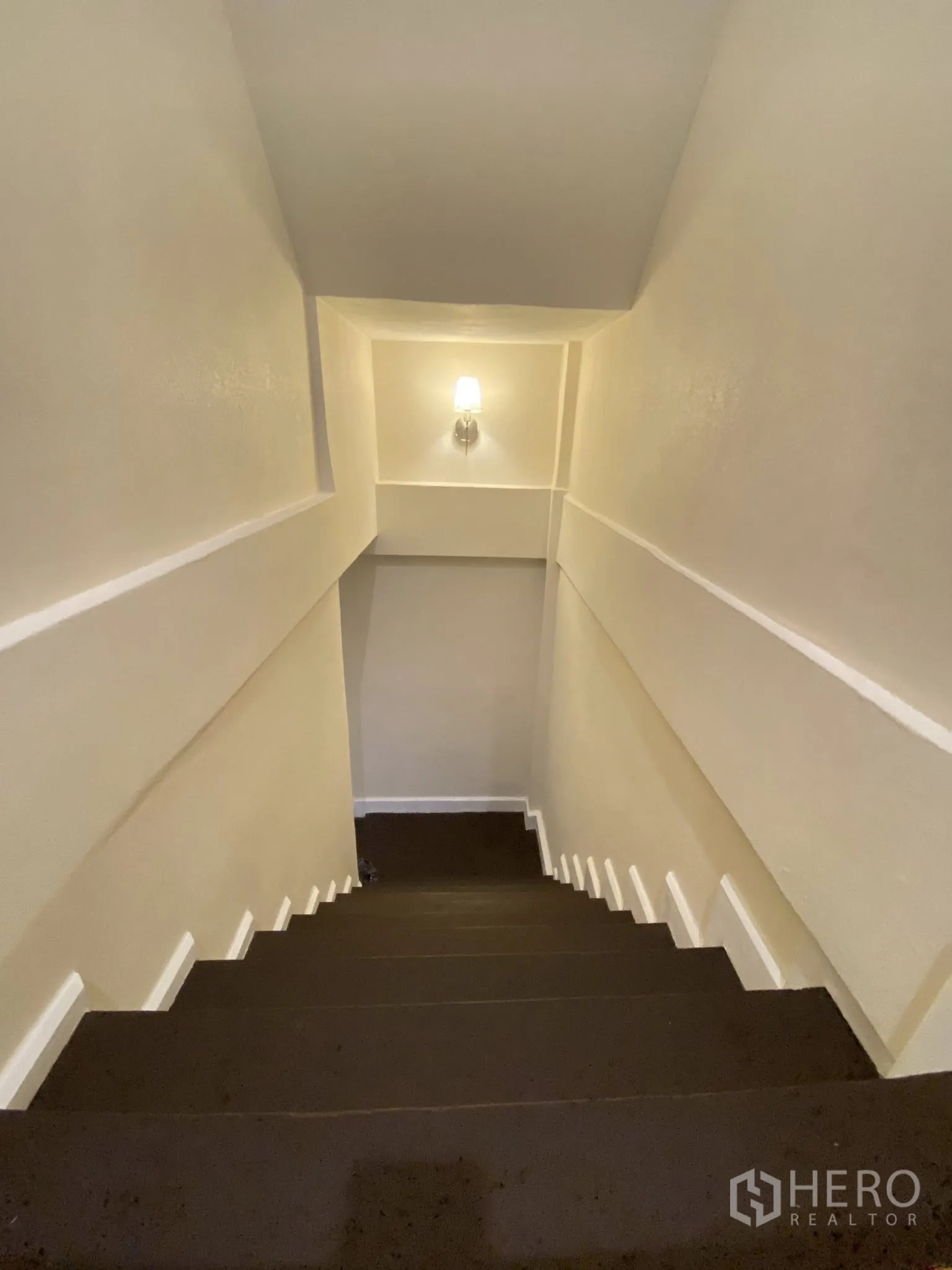 Home Office for rent in Pathum Wan, Bangkok - Well‑lit staircase with wall sconce and white trim leading to the lower floor.
