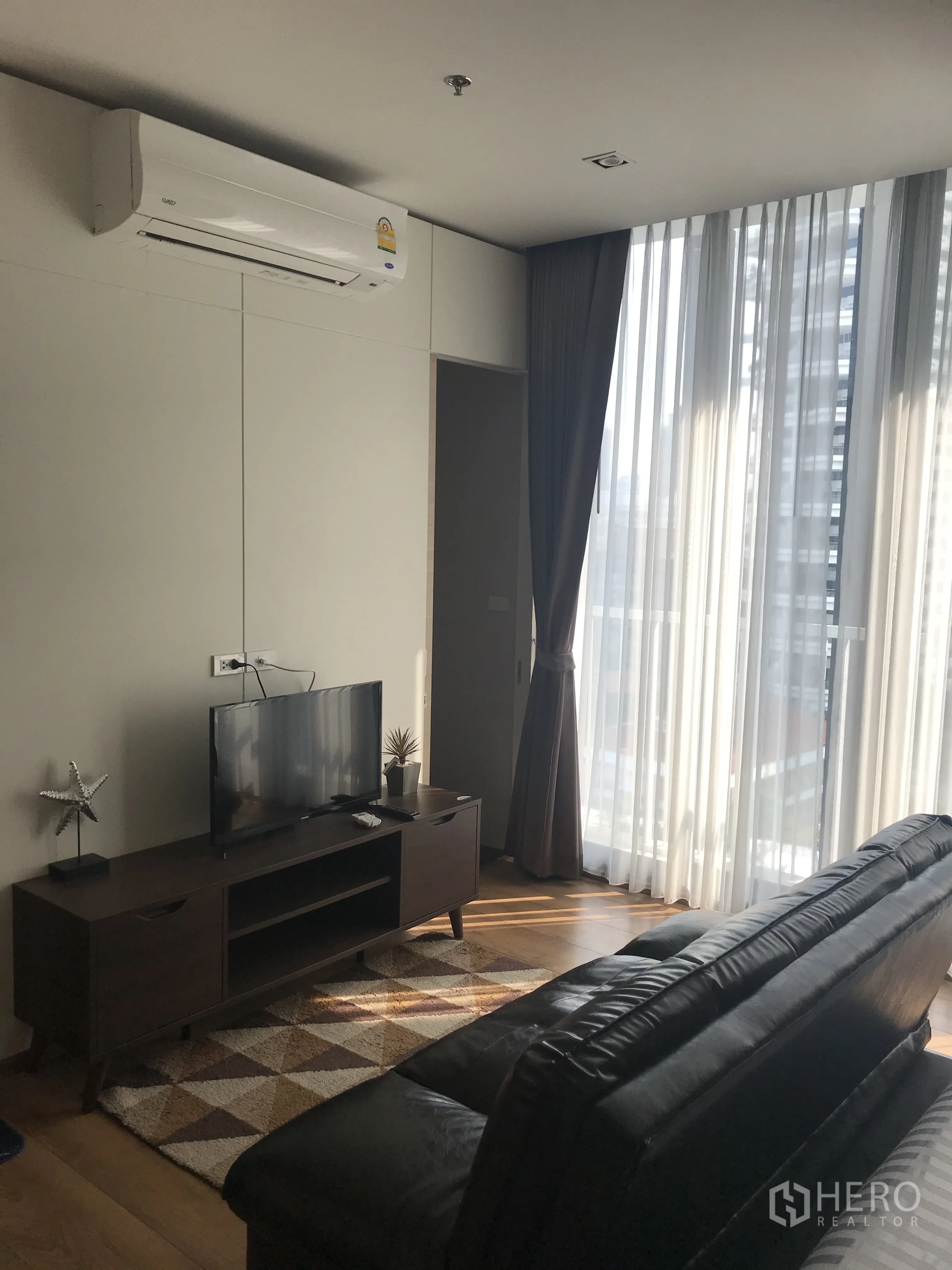 Condominium for sale in Khlong Toei, Bangkok - Living zone with AC unit, TV console, leather sofa, and bright windows.