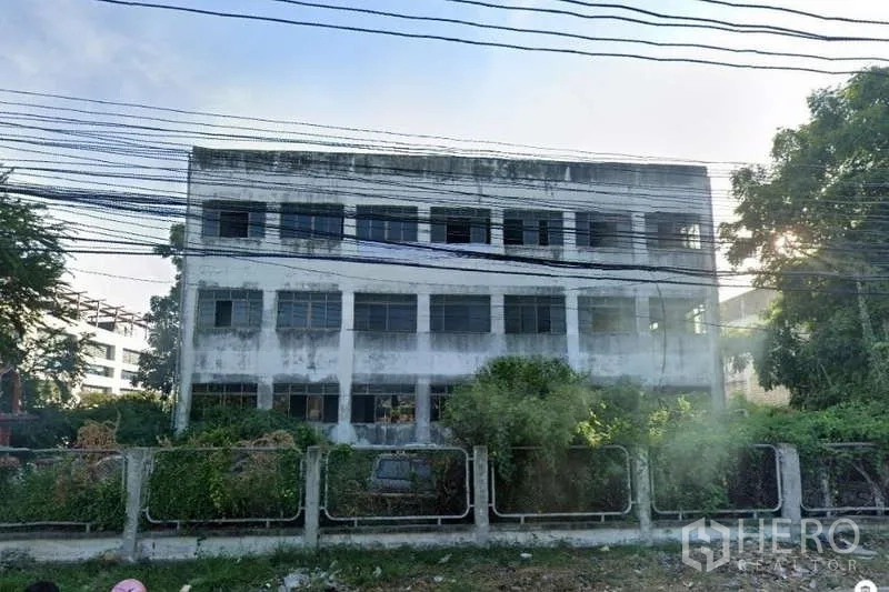 ที่ดิน ขายในLat Krabang, Bangkok - ด้านหน้าอาคารโรงงานเก่าพร้อมพุ่มไม้รกและสายสื่อสารพาดผ่าน