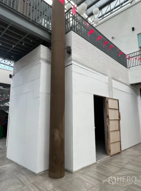 零售空间 出租在Khlong Toei, Bangkok - 白色墙面的拐角铺面，敞开门口，上方可见夹层与彩旗。