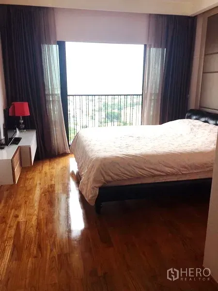 Condominium for rent or sale in Watthana, Bangkok - Cozy bedroom with wood flooring and a wide window offering a city outlook.