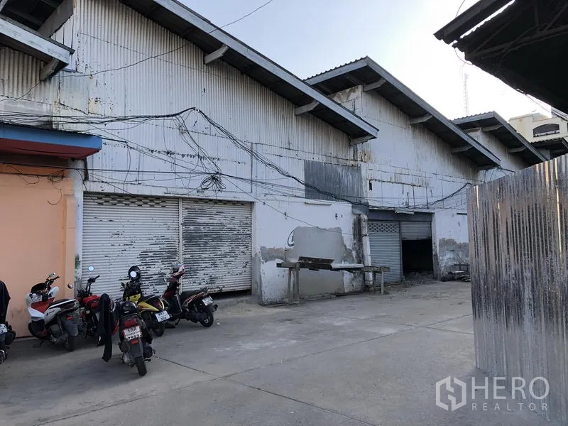 พื้นที่ขายปลีก ให้เช่าในKhlong Toei, Bangkok - ด้านหน้าอาคารเมทัลชีท มีประตูม้วนหลายจุดและลานโหลดของ พร้อมมอเตอร์ไซค์จอด