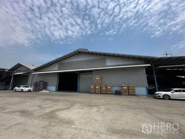 货栈 出租在Bang Pa-in, Phra Nakhon Si Ayutthaya - 仓库外立面斜角视图，可见装卸区、停放车辆和晴朗天空。