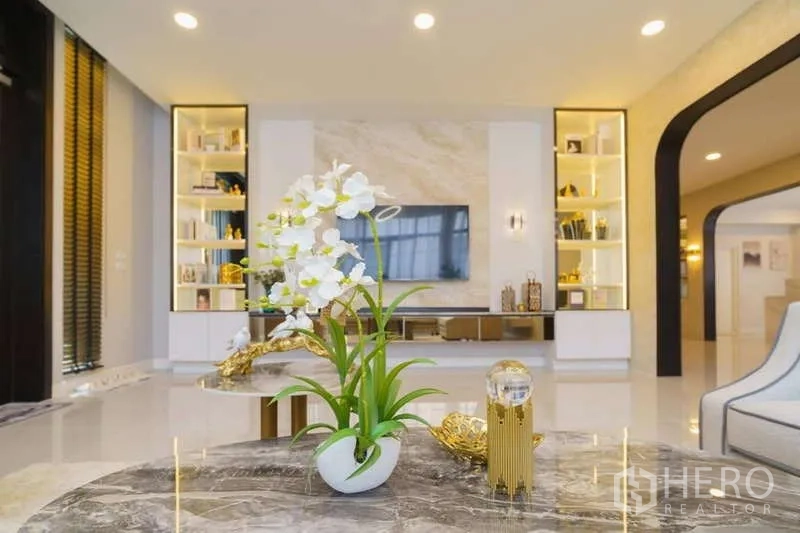 Detached House for rent or sale in Bang Phli, Samut Prakan - Coffee table with orchid centerpiece facing TV and display shelves in the living room.