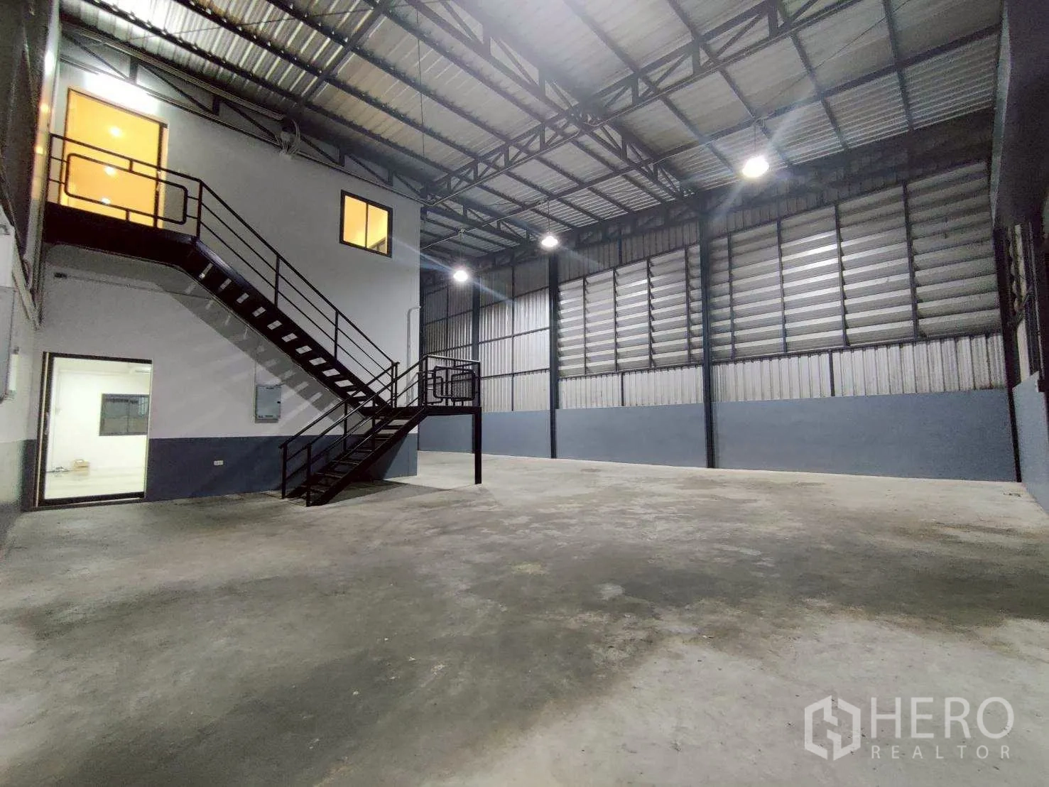 โกดัง for rent in Lam Luk Ka, Pathum Thani - ภาพรวมภายในโกดังหลังคาสูง มีห้องชั้นลอยและไฟสว่าง.