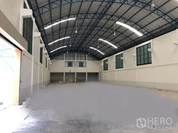 Factory for rent in Samut Prakan - Spacious factory warehouse interior with high arched steel roof, bright lighting and a mezzanine office at the far end.