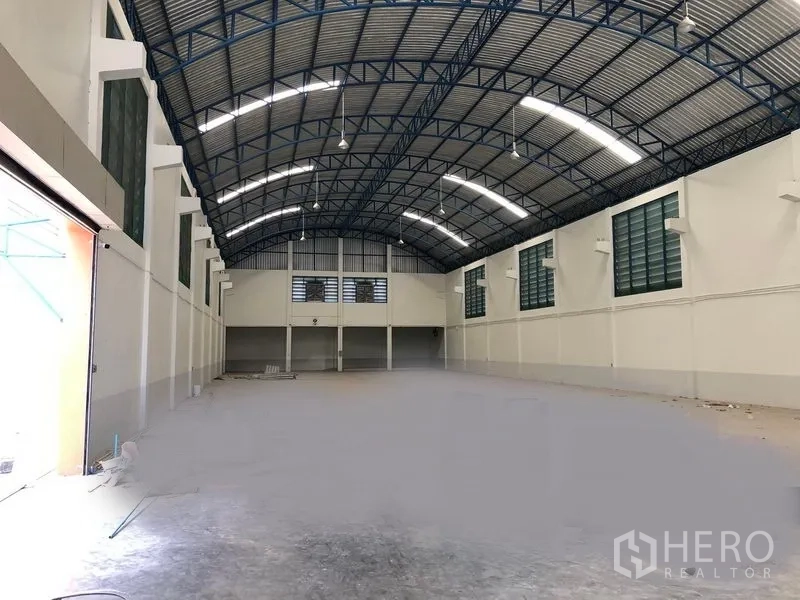 Factory for rent in Samut Prakan - Spacious factory warehouse interior with high arched steel roof, bright lighting and a mezzanine office at the far end.