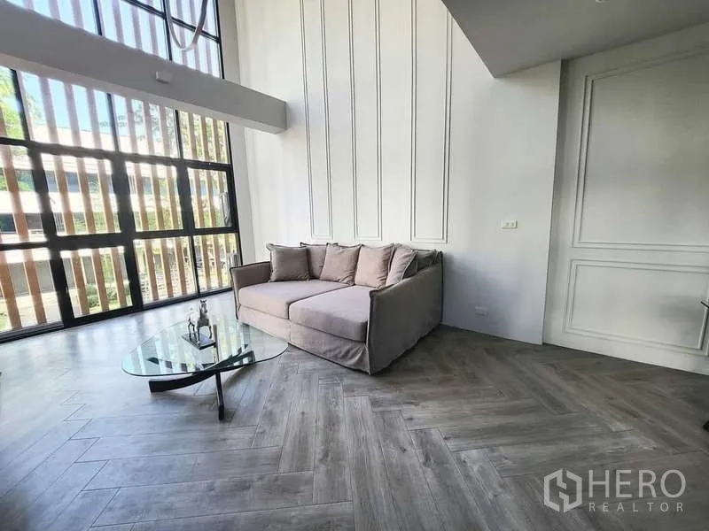 联排别墅 出租在Watthana, Bangkok - 客厅落地窗、装饰墙板与木纹人字拼地板。