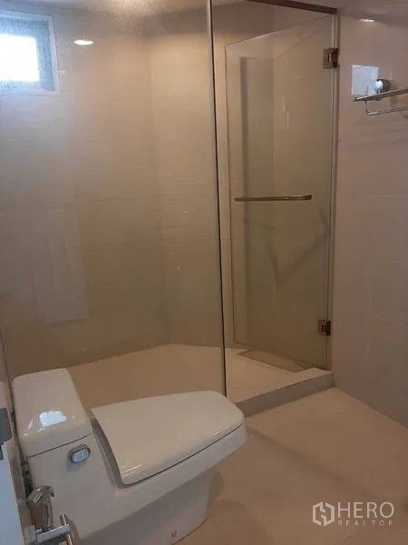 Condominium for rent or sale in Huai Khwang, Bangkok - Bathroom with glass-enclosed shower, modern toilet, and light tiles.