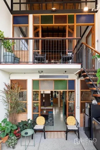 Townhouse for rent in Pathum Wan, Bangkok - Loft-style courtyard with wood-framed windows, balcony seating and a steel staircase.