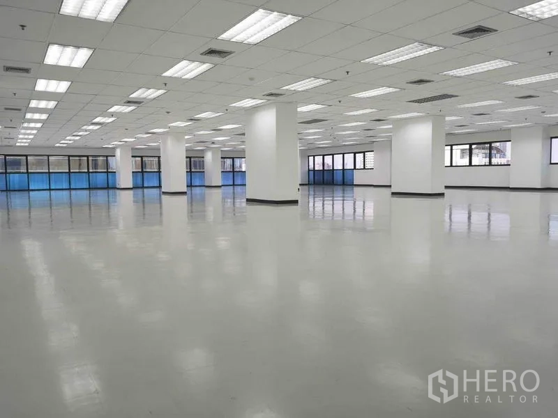 办公空间 出租在Phaya Thai, Bangkok - 无家具的办公大厅，等距立柱、吊顶灯及窗旁蓝色遮阳。