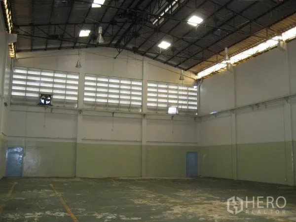 Factory for rent in Bang Sao Thong, Samut Prakan - Wide warehouse interior featuring skylights, hanging industrial lights, and marked floor lanes.