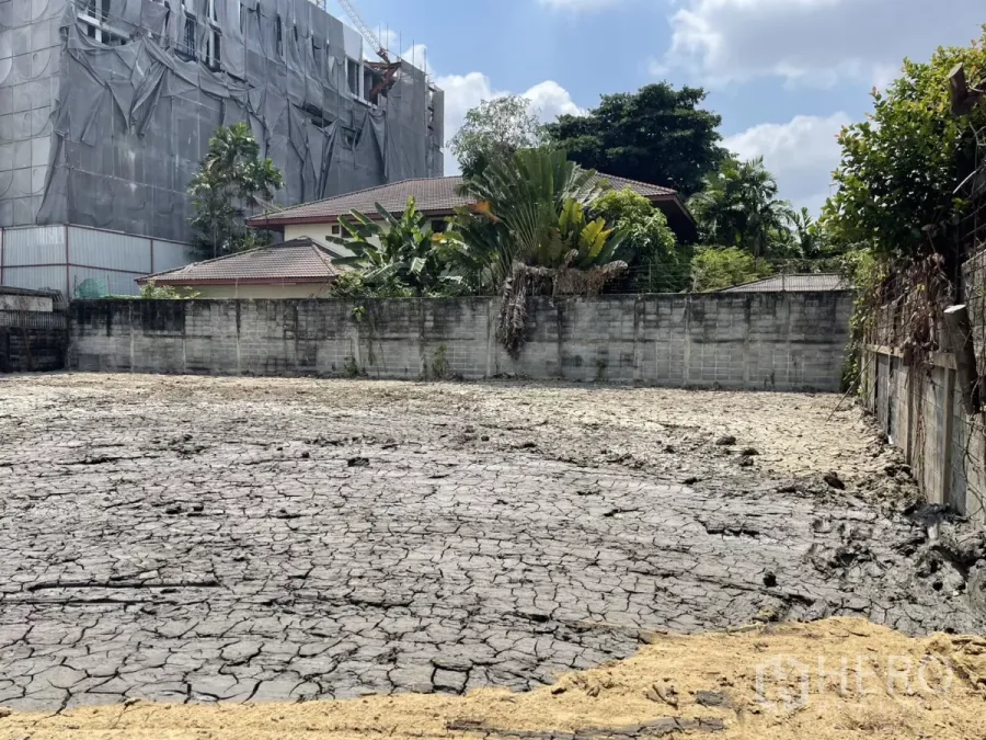 ที่ดิน ขายในPhra Khanong, Bangkok - ที่ดินเปล่าล้อมกำแพงในพระโขนง ใกล้ BTS ปุณณวิถี พื้นดินแตกระแหง มีบ้านและต้นไม้รอบ ๆ และอาคารที่กำลังก่อสร้างด้านหลัง
