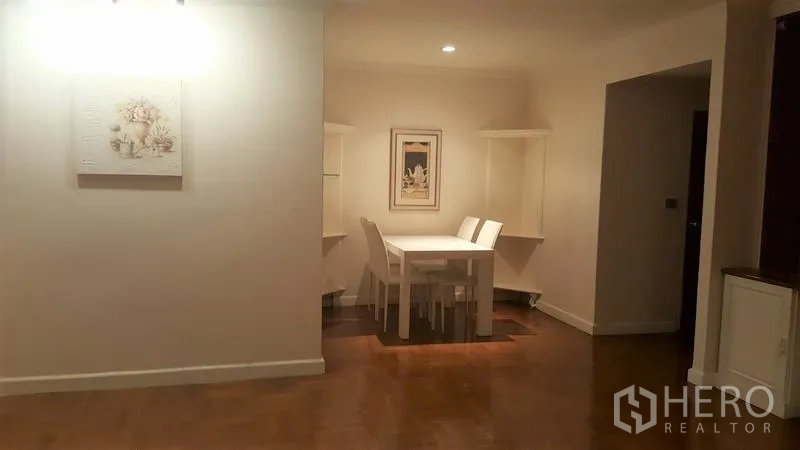 Condominium for rent in Watthana, Bangkok - Cozy dining nook with a white table and chairs, wall art, and warm lighting over wooden floors.