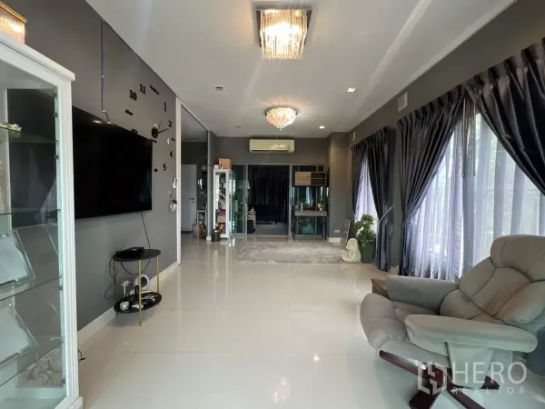 บ้าน ให้เช่าหรือขายในLat Krabang, Bangkok - พื้นที่ห้องรับแขกยาว ผนังสีเทาพร้อมทีวีติดผนังและโคมไฟคริสตัล