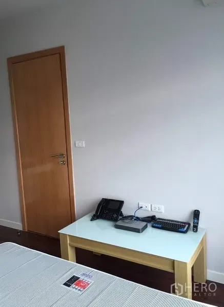 公寓 出租或出售在Ratchathewi, Bangkok - 卧室一角，浅木门与摆放电子设备的小型桌台。