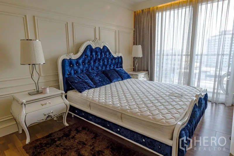 Condominium for rent in Watthana, Bangkok - Bedroom with blue velvet bed, twin bedside tables and floor-to-ceiling windows offering skyline views.