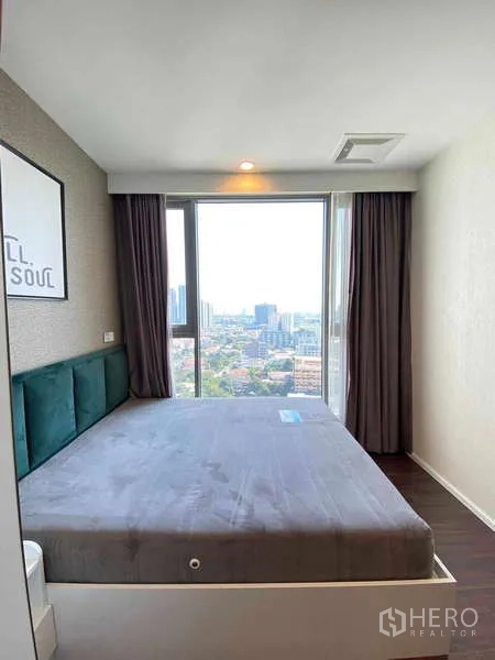 Condominium for rent - Bedroom with large window, city skyline view, dark curtains and padded headboard.