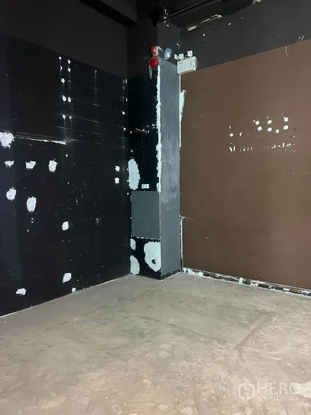 零售空间 出租在Watthana, Bangkok - 未装修的店铺一角，深色特色墙面带修补痕迹，外露管线与水泥地面。