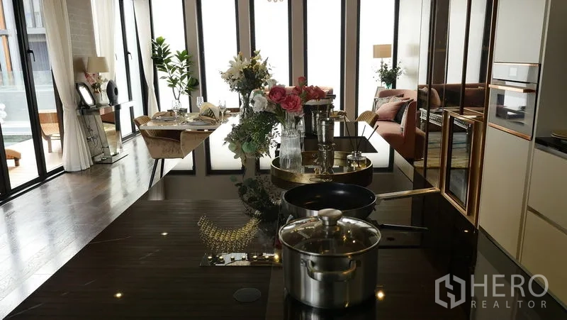 独立式住宅 出售在Prawet, Bangkok - 近景：高光厨房中岛，嵌入式炉台、锅具与花艺装饰。