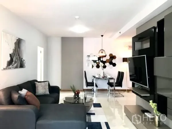 Condominium for rent or sale in Huai Khwang, Bangkok - Spacious lounge facing a media wall, sectional sofa, and dining nook in the background.