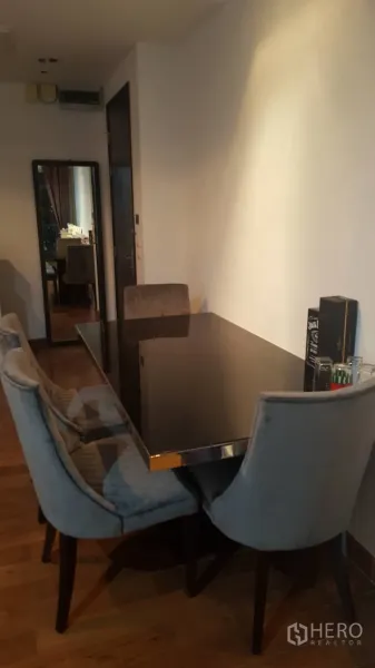 คอนโด ให้เช่าในPathum Wan, Bangkok - มุมรับประทานอาหารพร้อมโต๊ะแก้วสีดำ เก้าอี้บุผ้า และพื้นไม้ในคอนโดสมัยใหม่