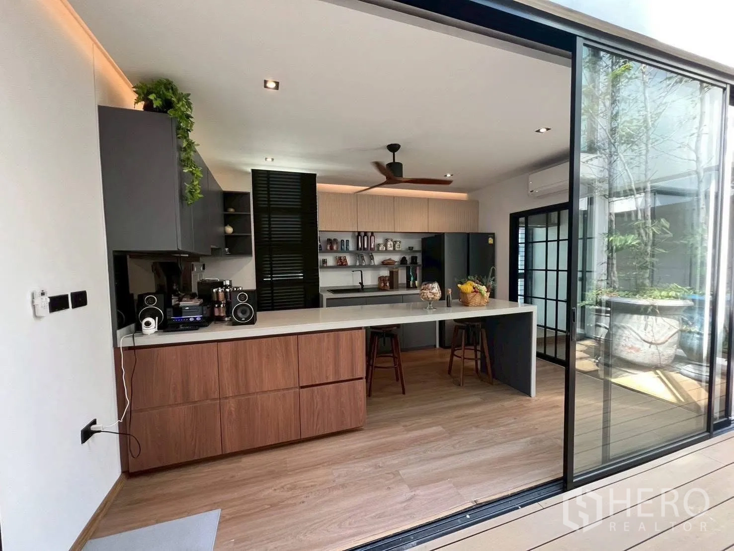 Home Office for rent or sale in Mueang Samut Prakan, Samut Prakan - Modern kitchen with island counter, bar stools, open shelving and sliding glass doors.