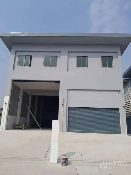货栈 出租或出售在Krathum Baen, Samut Sakhon - 仓库正立面，灰色外墙，双卷帘门与车道入口。