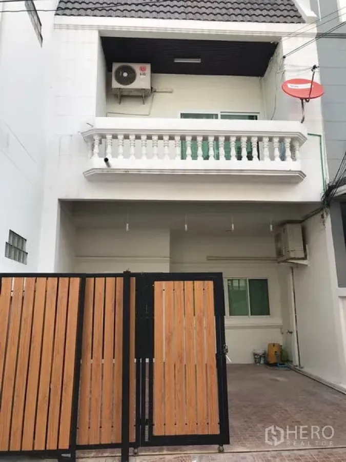 ทาวน์เฮาส์ ให้เช่าหรือขายในPhra Khanong, Bangkok - ด้านหน้าทาวน์เฮ้าส์หลายชั้นสีขาว พร้อมระเบียงและโรงจอดรถมีกำแพงรั้ว